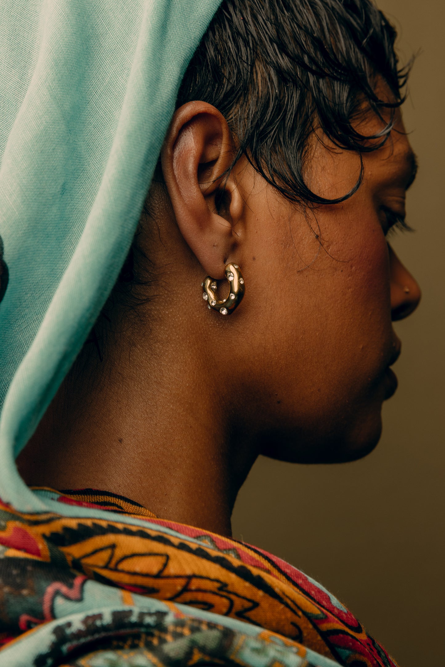 A person viewed from the side wearing a headscarf and large hoop earrings.