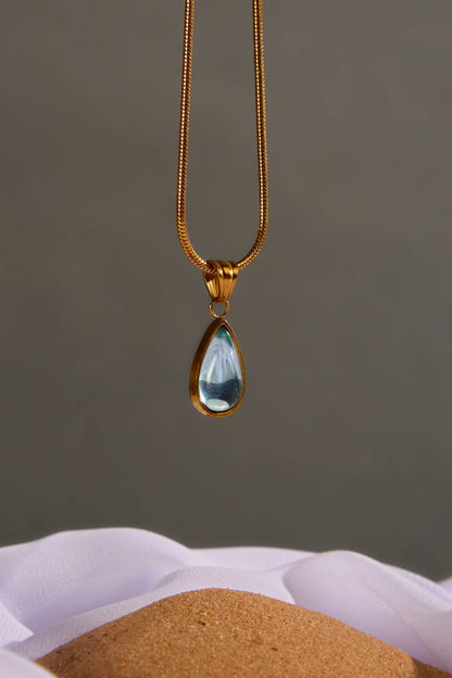 Gold necklace with a teardrop-shaped pendant on a neutral background