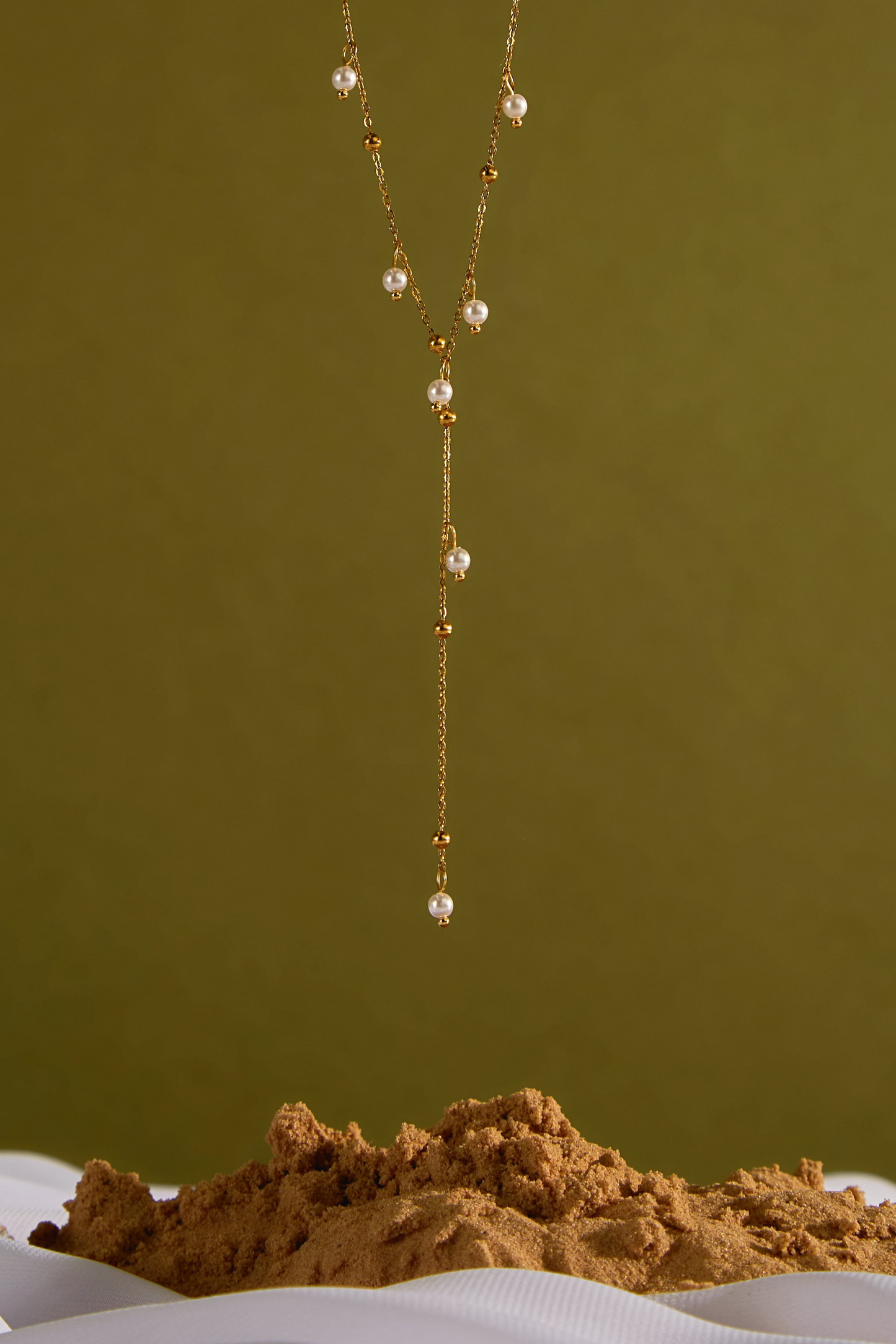 Long necklace with pearls on a textured surface against a green background