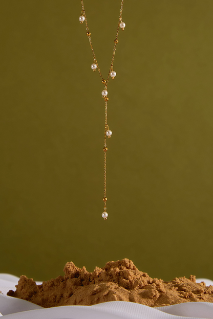 Long necklace with pearls on a textured surface against a green background
